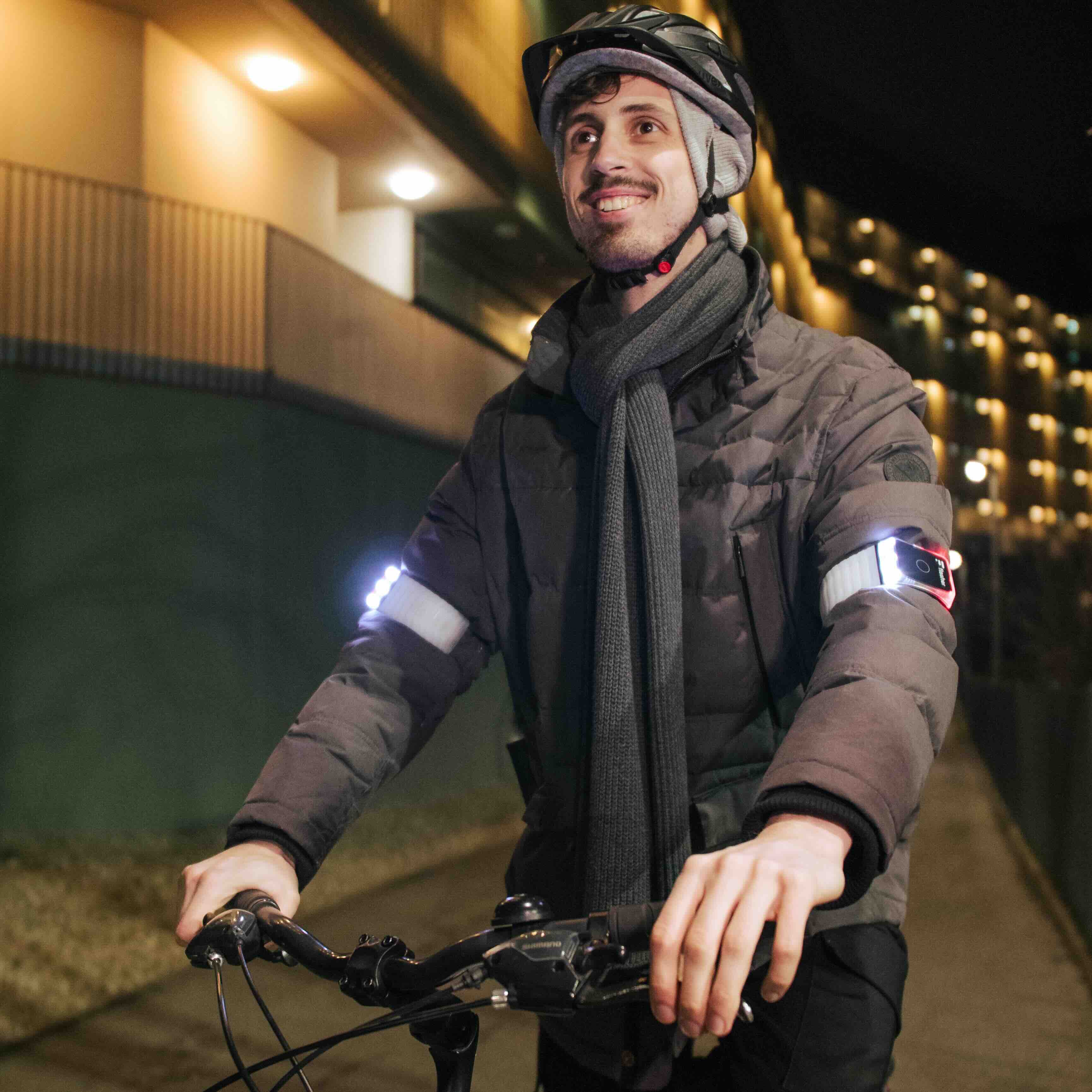 Radfahrer in dunkler Winterkleidung mit Helm und Flasher Blinker Armbändern, die weiß und rot leuchten.