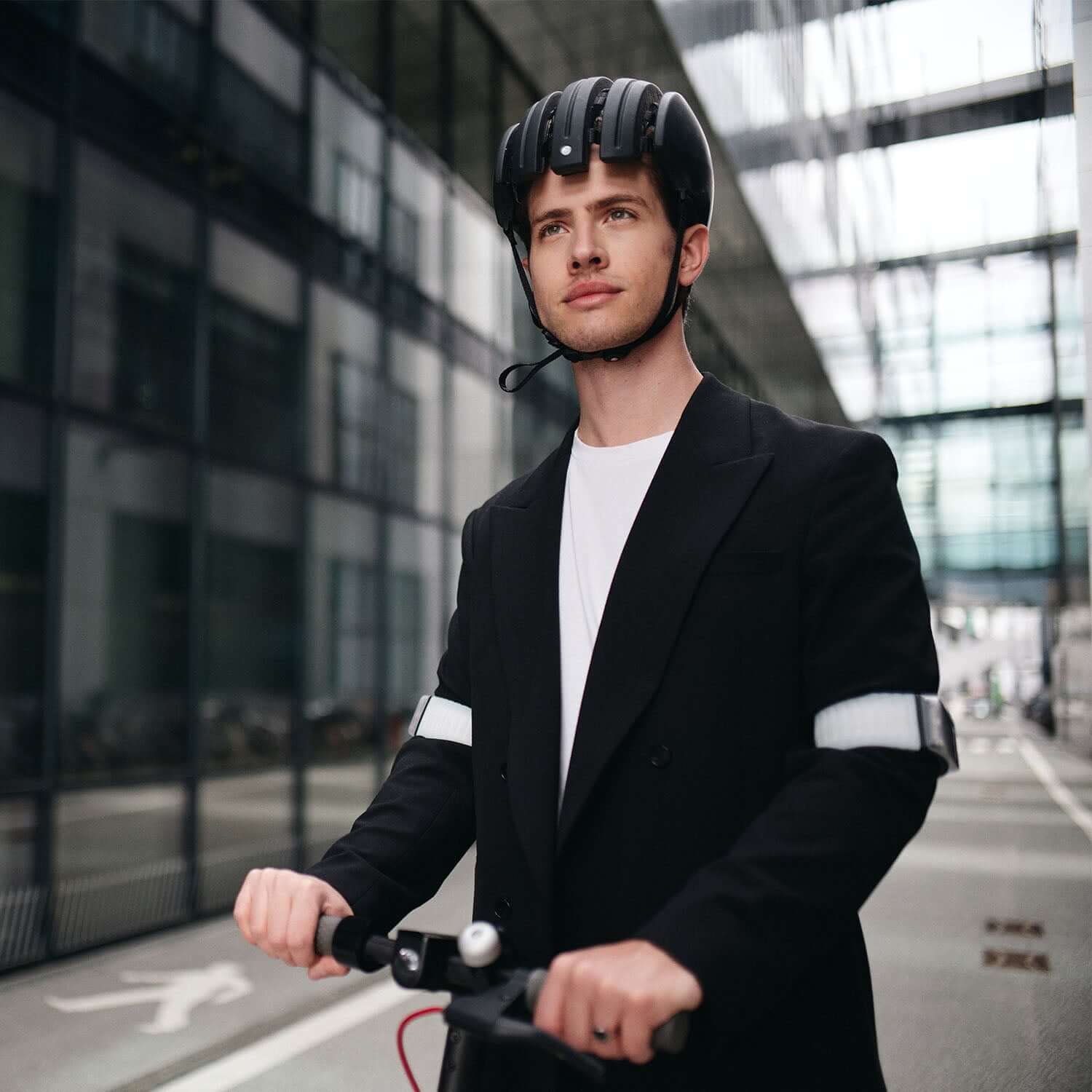 Junger Mann in Anzug auf E-Scooter mit zwei Flasher Armbändern.