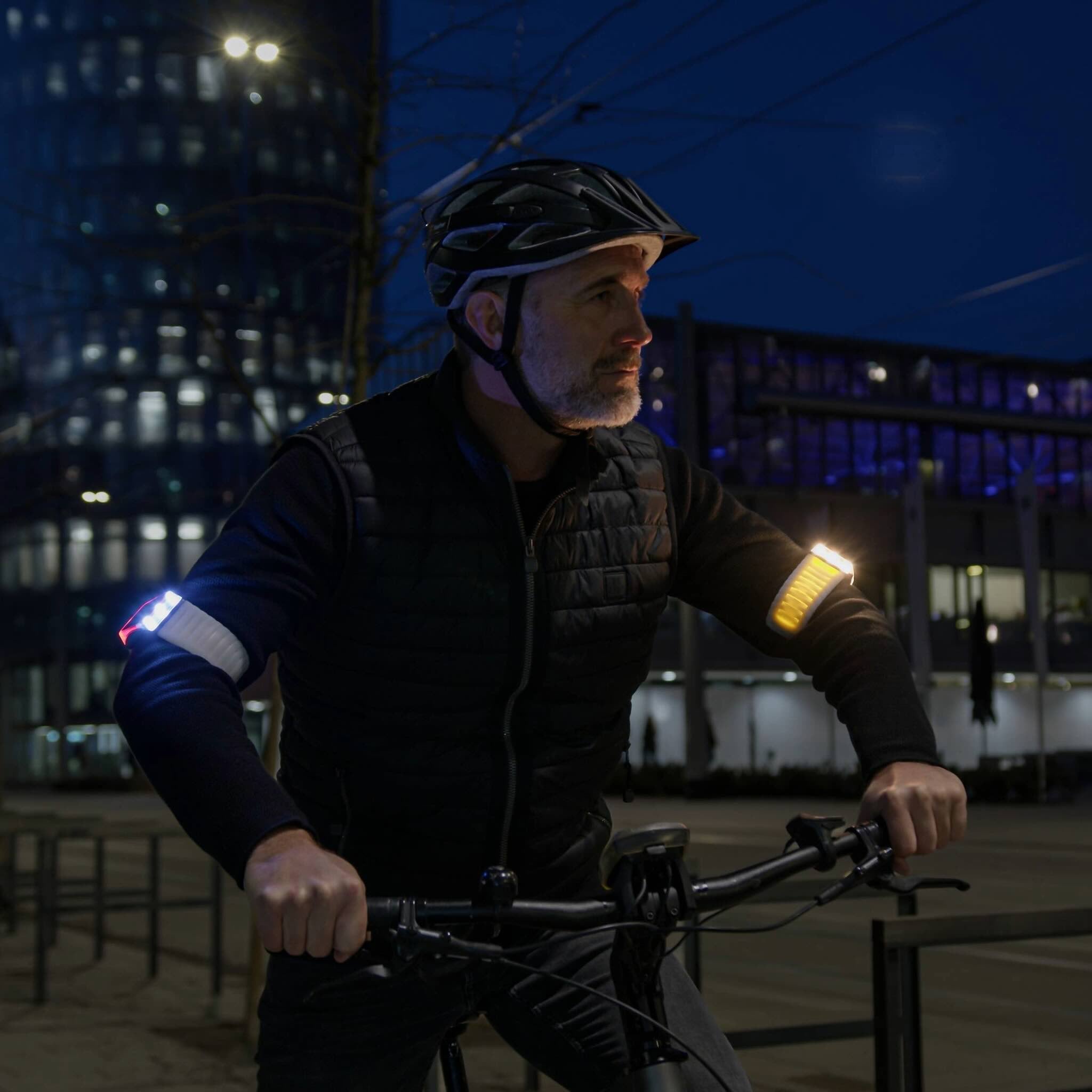 Radfahrer abends mit brilliant hellen Flasher Armbändern von vorne. Links weißes Licht, rechts gelber Blinker.