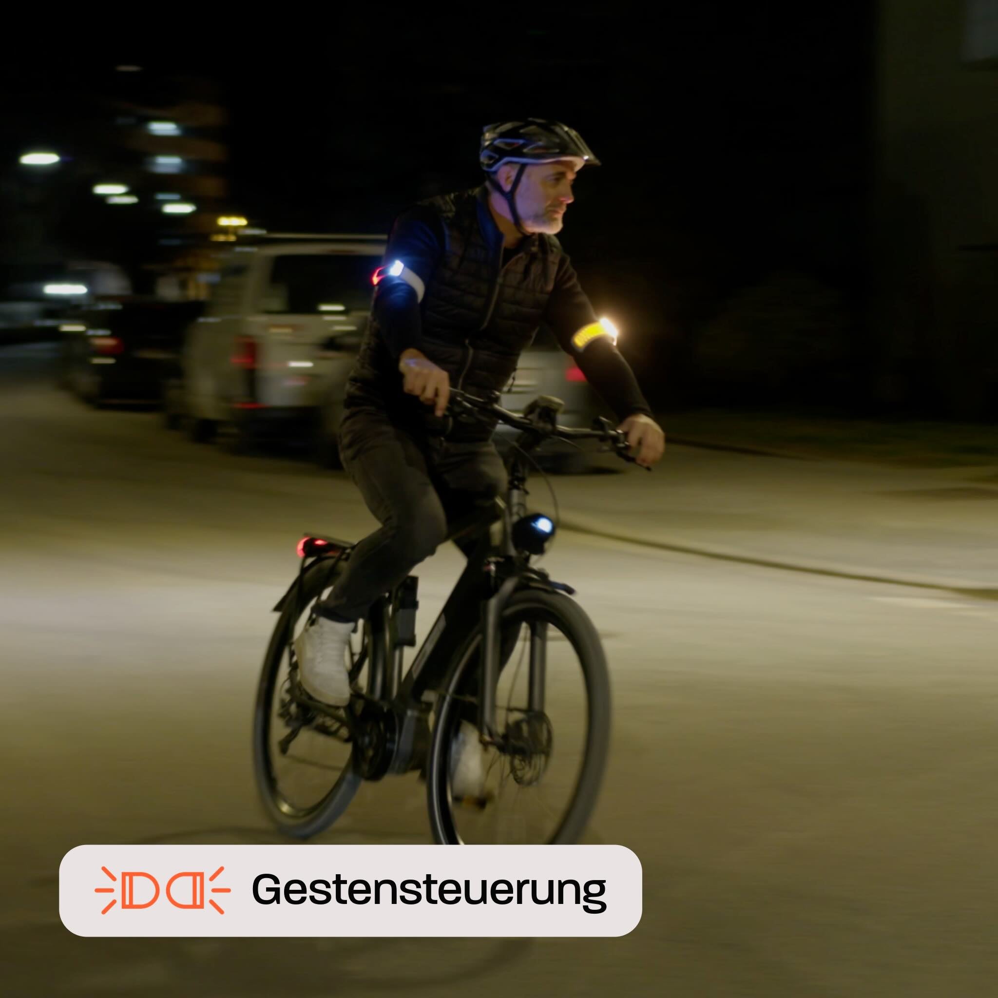 Radfahrer mit Flasher abends beim Abbiegen, Hände am Lenker, linkes Armband blinkt gelb. Text "Gestensteuerung"