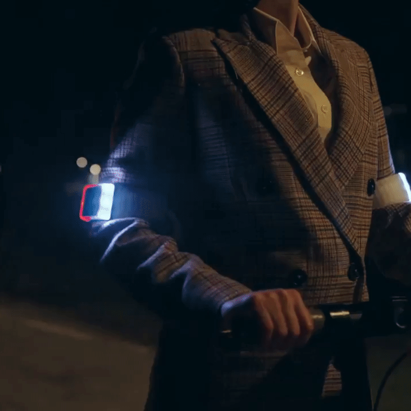 Eine Person am E-Scooter, nachts, die den hellen gelben Blinker von Flasher durch ein leichtes Schwenken des Ellbogens aktiviert.