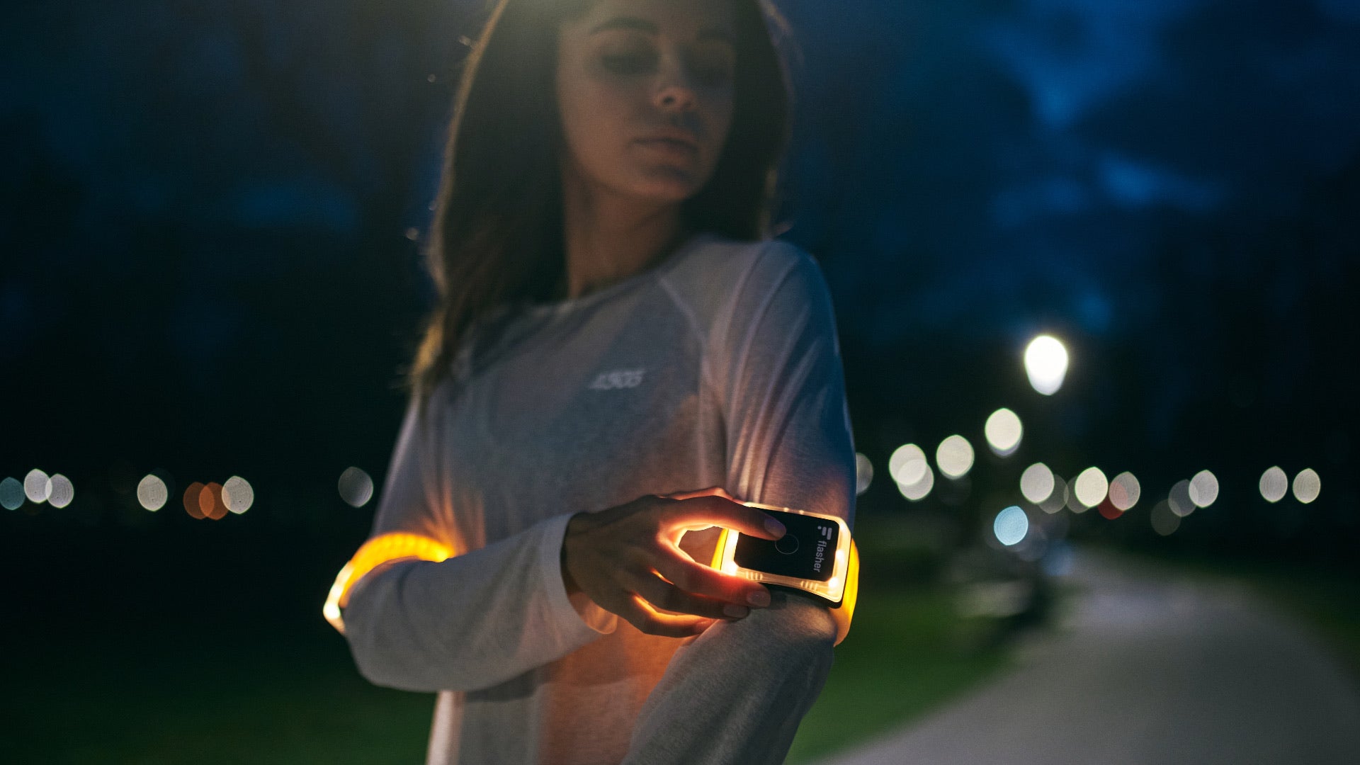 Junge Frau in Sportkleidung nachts, die ihre rundum hell gelb leuchtenden Flasher Armbändern einschaltet.