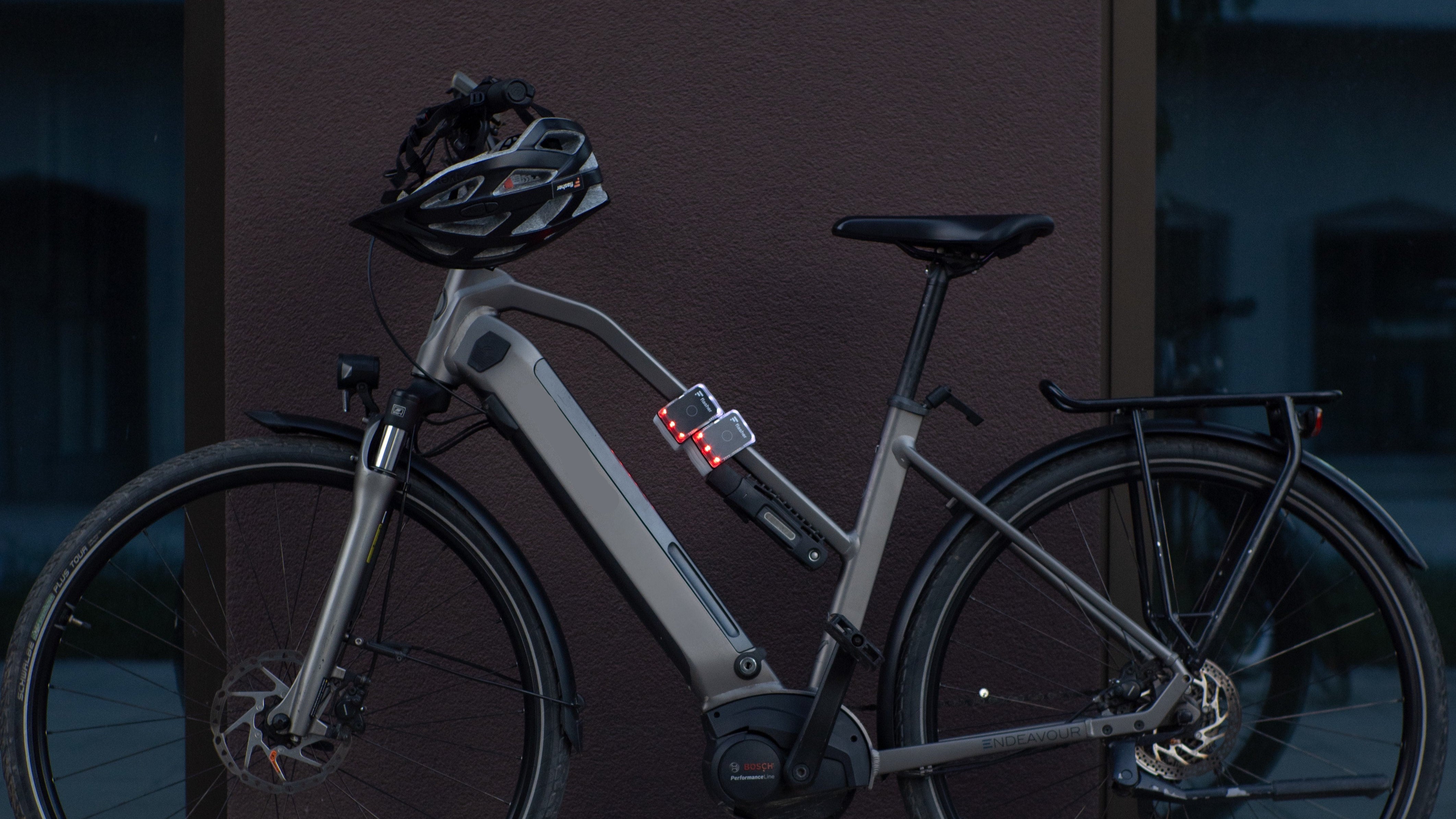 E-Bike lehnt mit Flasher am Rahmen an einer braunen Hauswand.