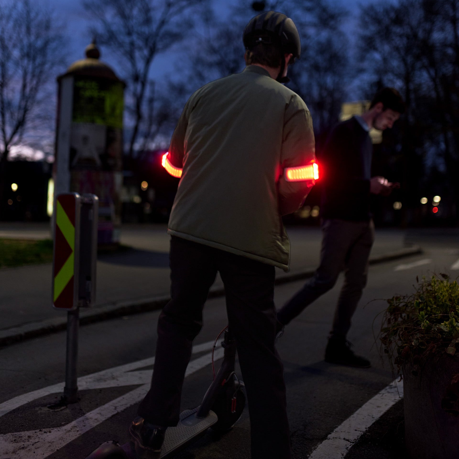 E-Scooter-Fahrer mit Flasher-Bremslicht, der vor Fußgänger nachts abbremst.