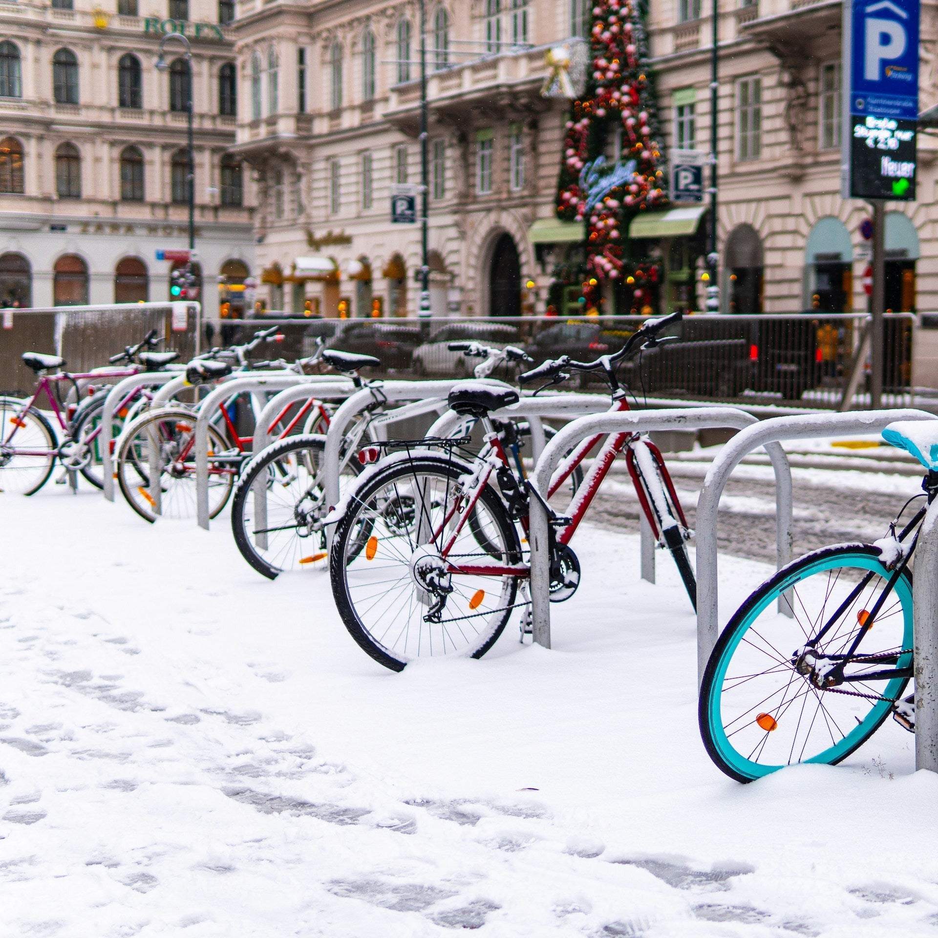 Eine bunte Reihe Fahrräder an Fahrradstädern, alle schneebedeckt.