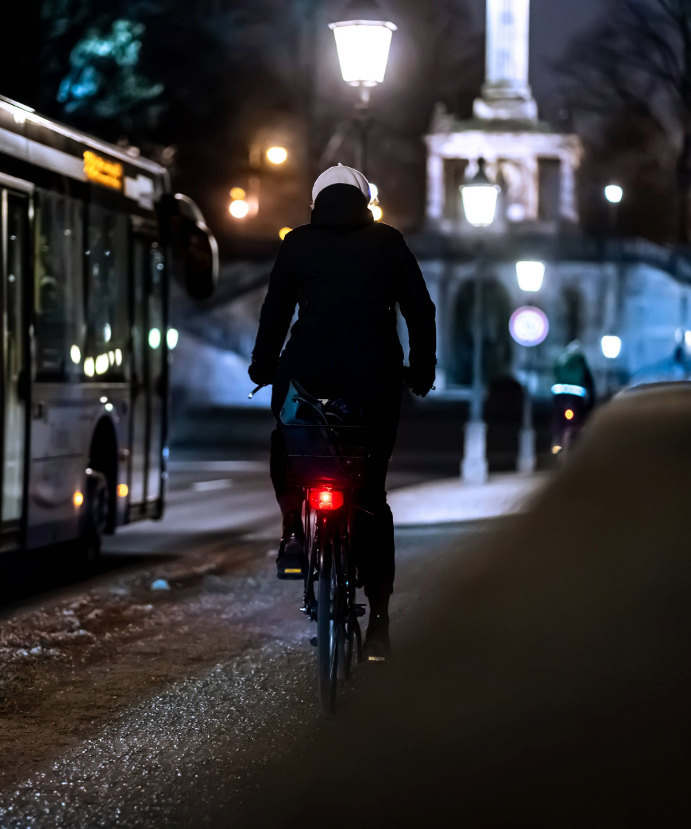 Eine Radfahrerin nachts mit dunkler Kleidung, die im Straßenverkehr schwer sichtbar ist.