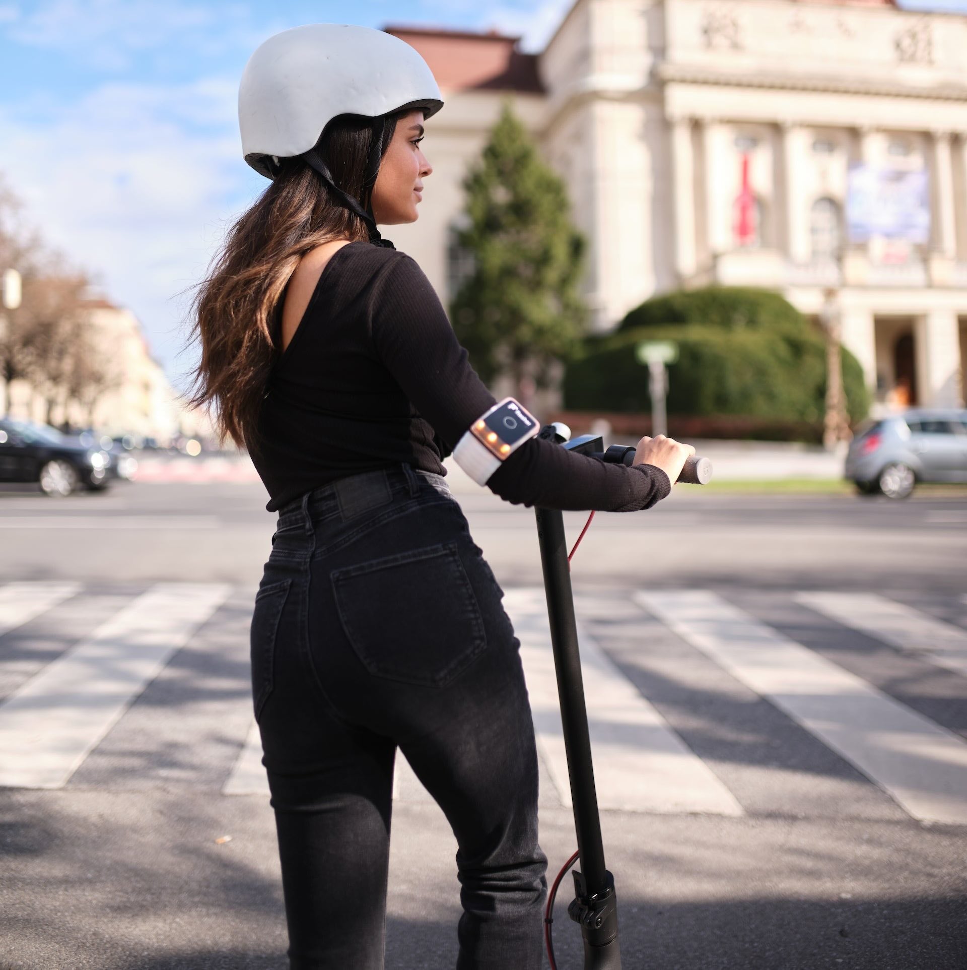 Junge Frau am E-Scooter tagsüber, mit klar sichtbaren, gelb leuchtendem Flasher Armband.